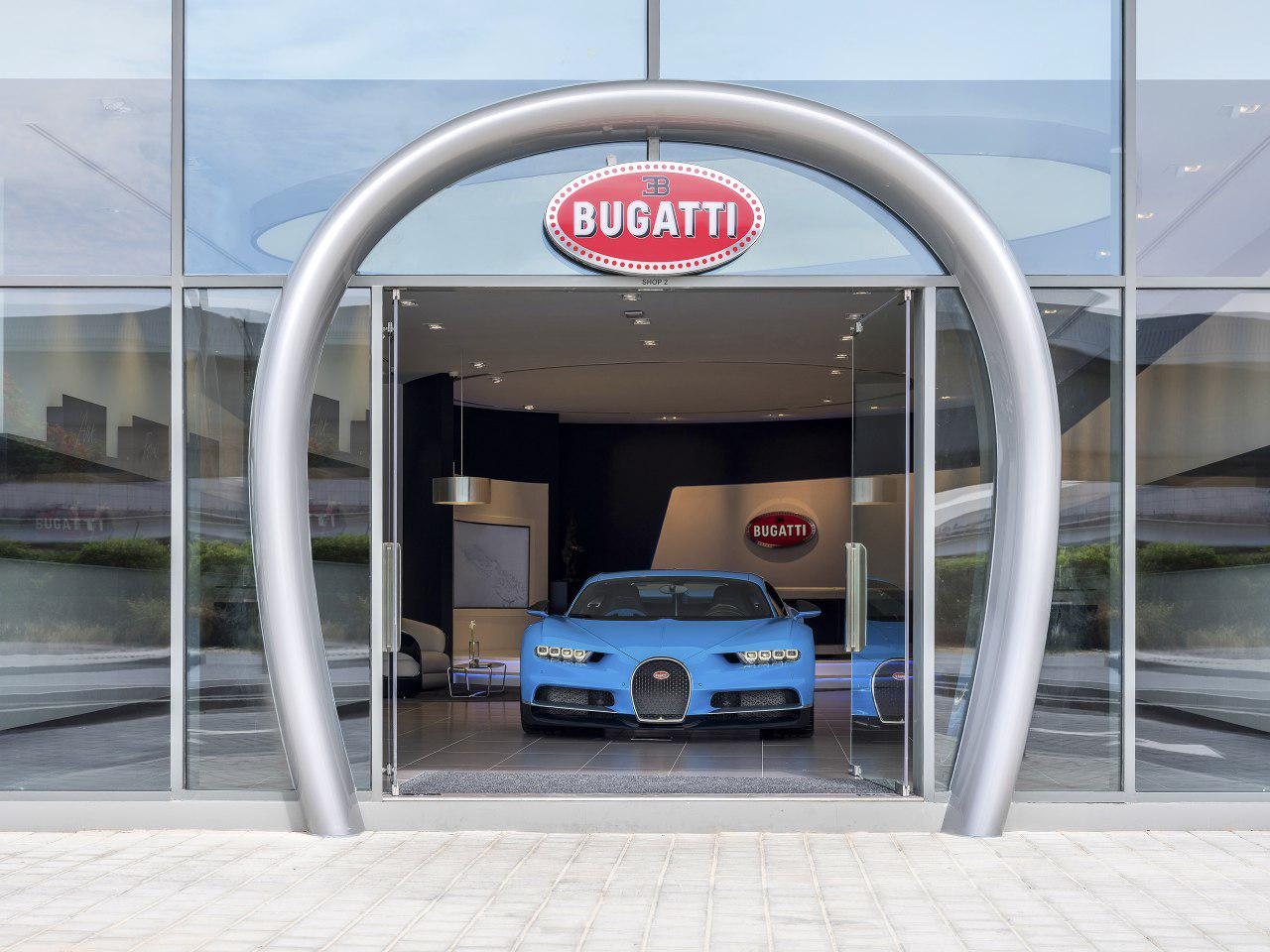 Bugatti showroom entrance framed by a chrome horseshoe, a blue Chiron inside